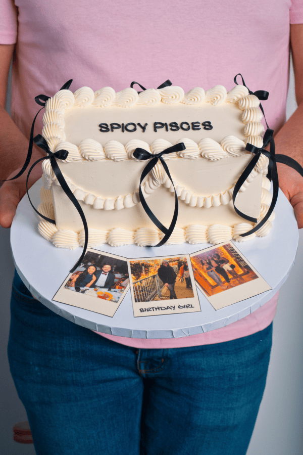 Cake shaped like a handbag with 'Spyoy Pisces' text, held by a person wearing a pink shirt and blue jeans.
