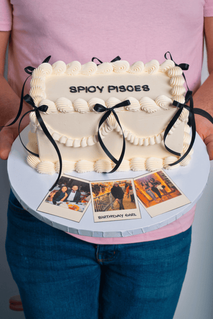 Cake shaped like a handbag with 'Spyoy Pisces' text, held by a person wearing a pink shirt and blue jeans.