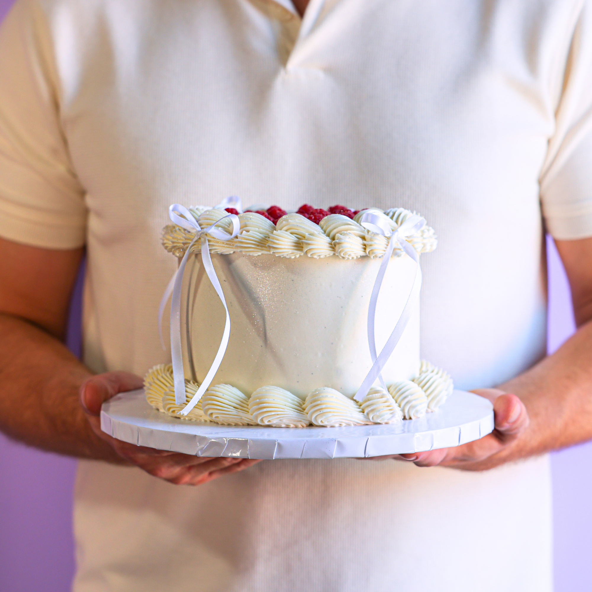 Person holding a small decorative cake with white frosting and red berries.