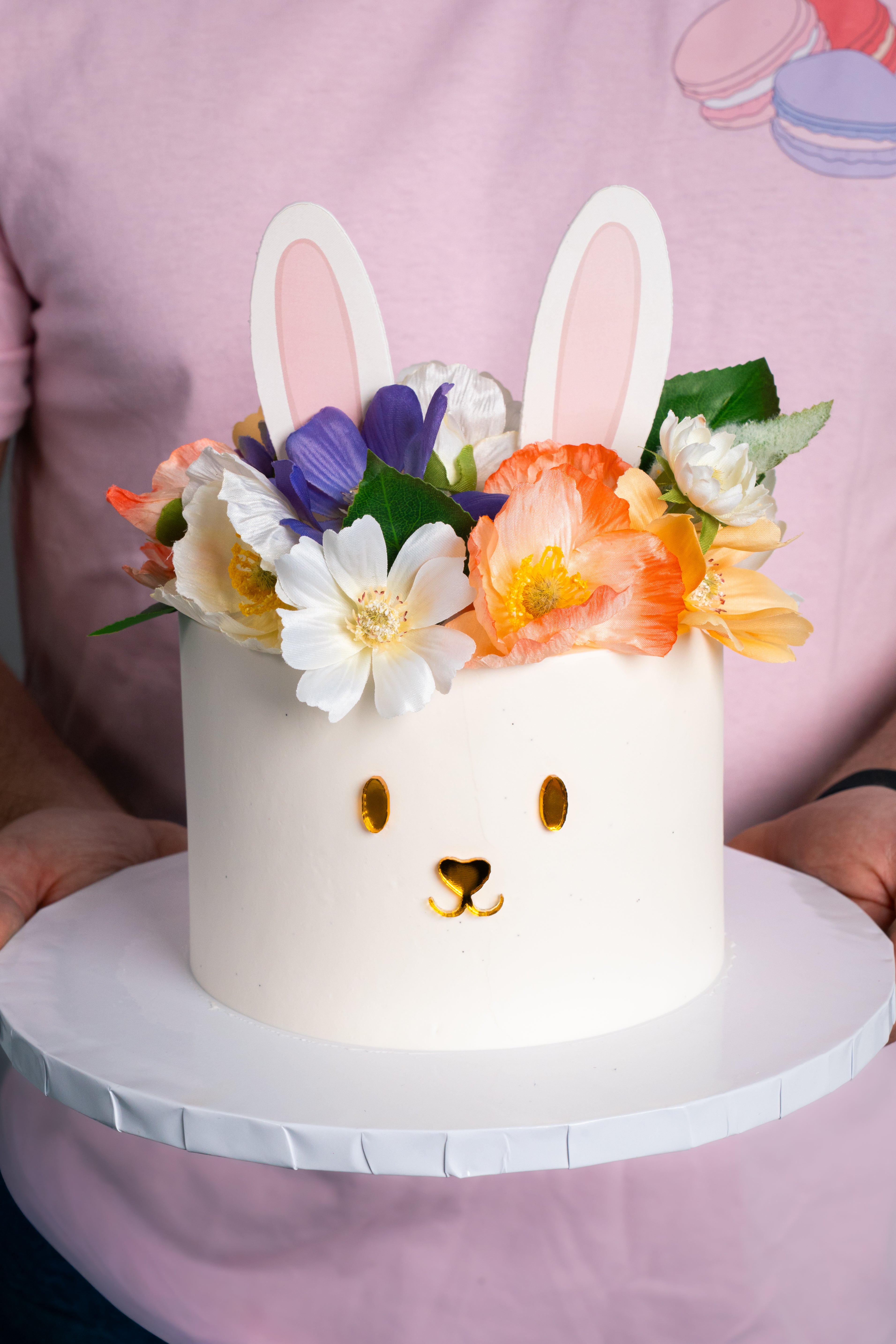 White cake decorated like a bunny with colorful flowers on a pink background