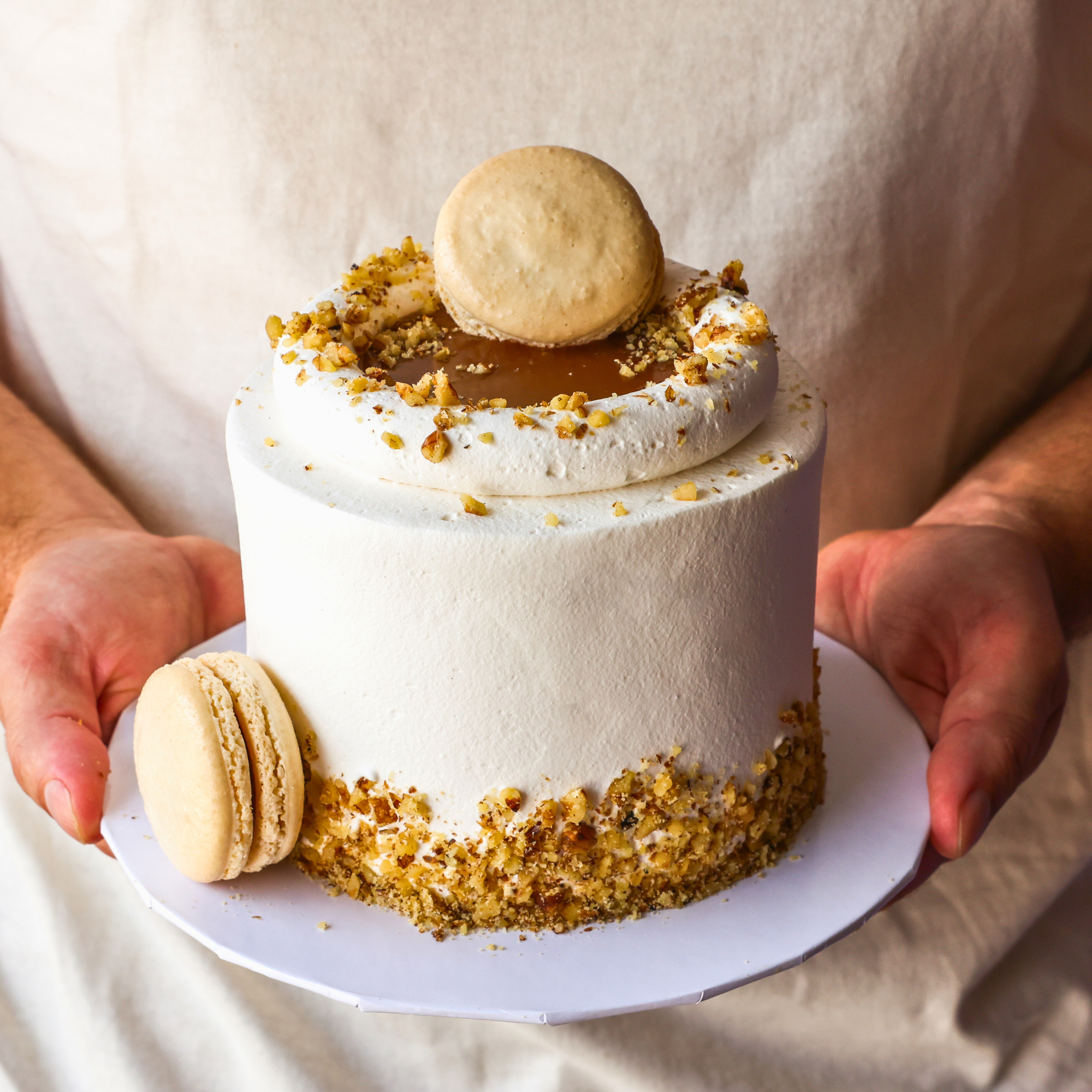 Small white cake with a macaron on top, held by a person