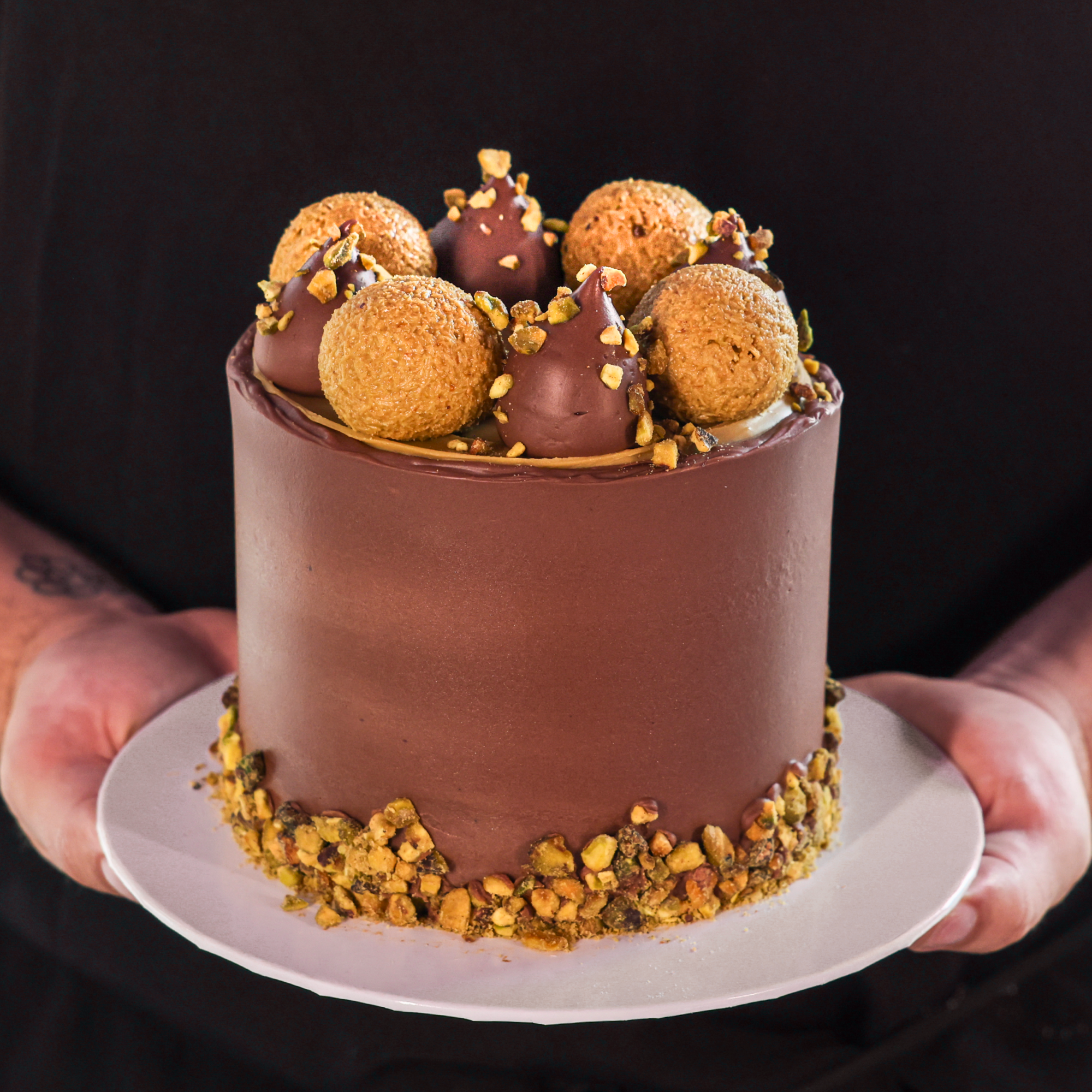 Chocolate cake with decorative elements held by a person against a black background