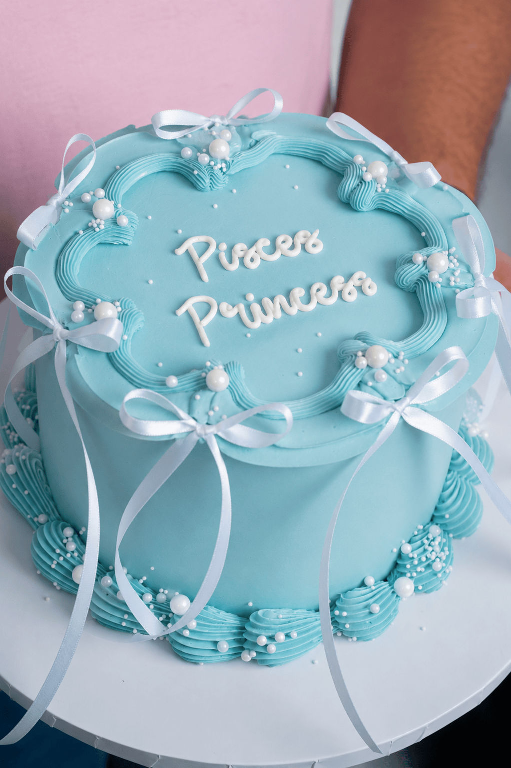 Light blue cake with 'Princess' text and decorative ribbons on a white plate.