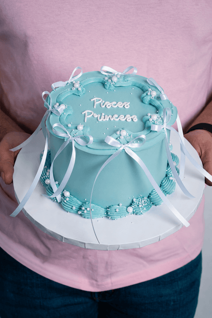 Blue cake with 'Princess' text held by a person wearing a pink shirt.