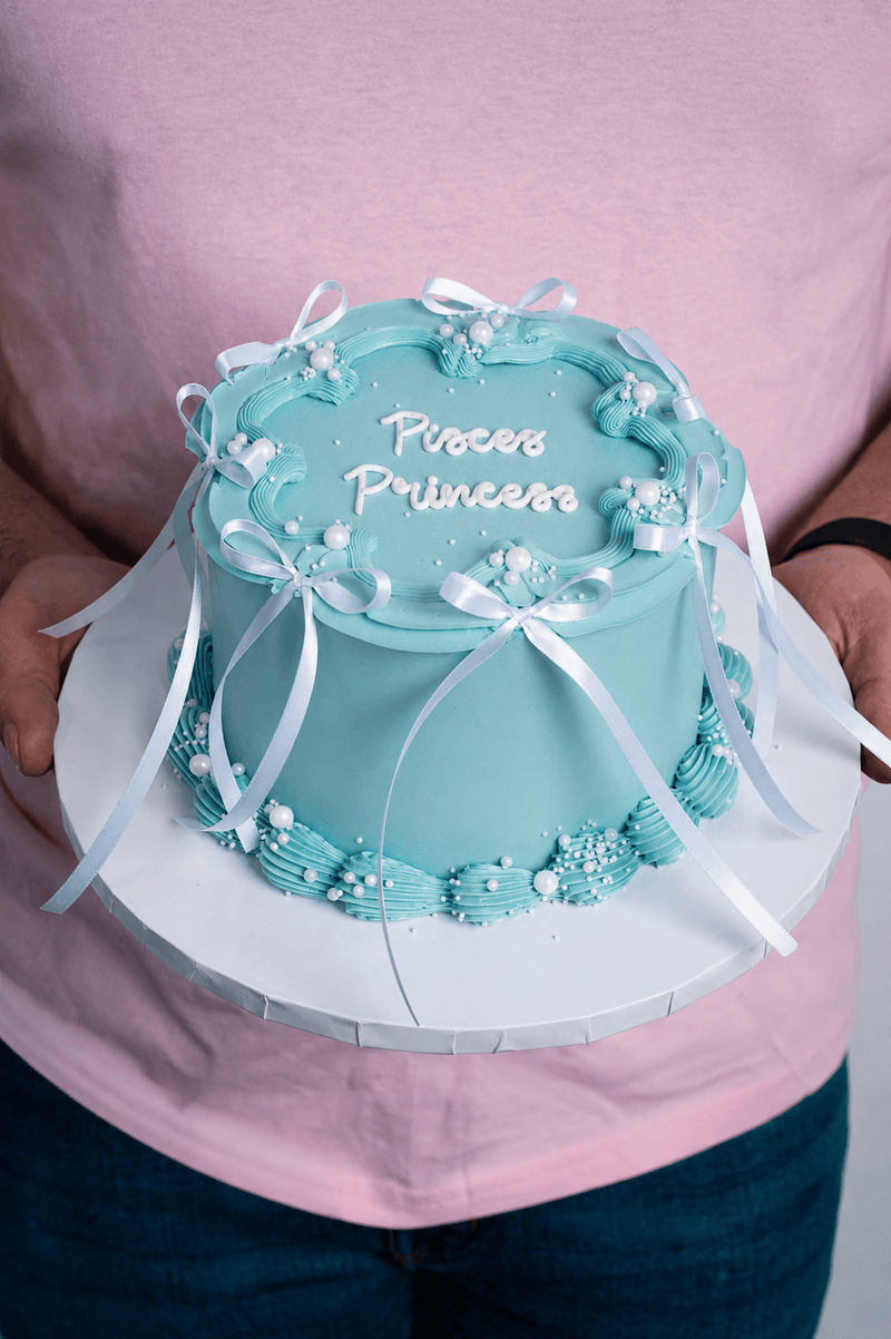 Blue cake with 'Princess' text held by a person wearing a pink shirt.