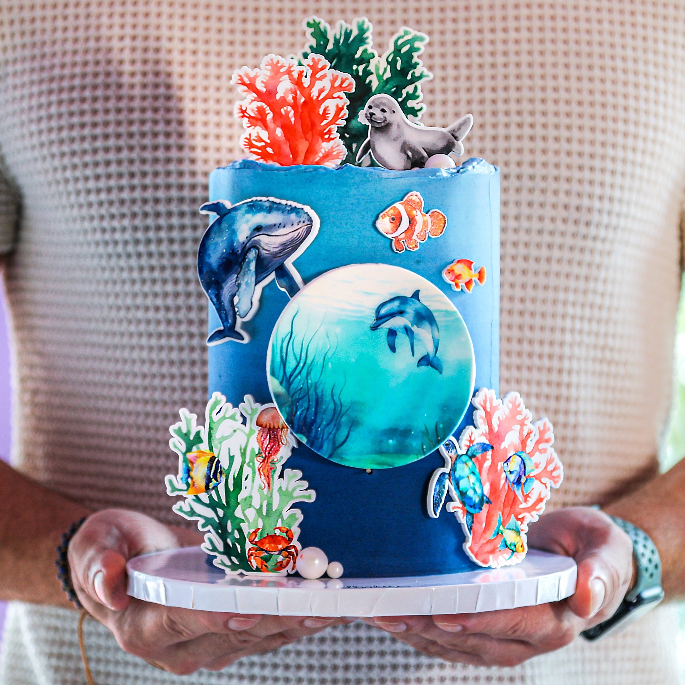 A decorated cake with ocean theme, including blue layers, white and blue fish, and coral reef details.
