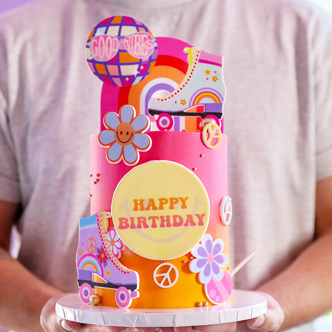 A colorful birthday cake with 'Happy Birthday' text, decorated with rollerskates, flowers, and the phrase 'Good Vibes'.