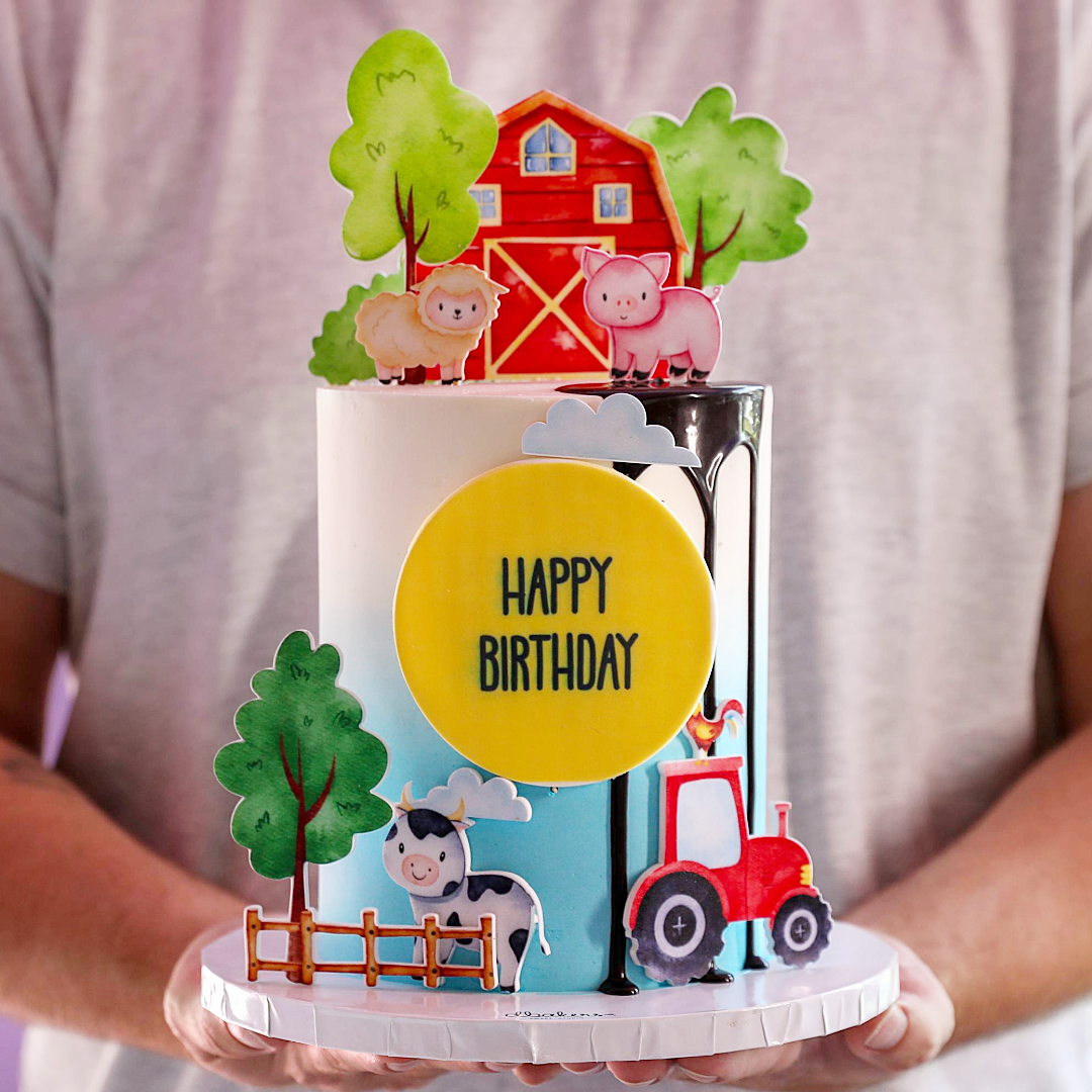 A decorated birthday cake with farm animals, including a pig, sheep, cow, and rooster, with a 'Happy Birthday' message.