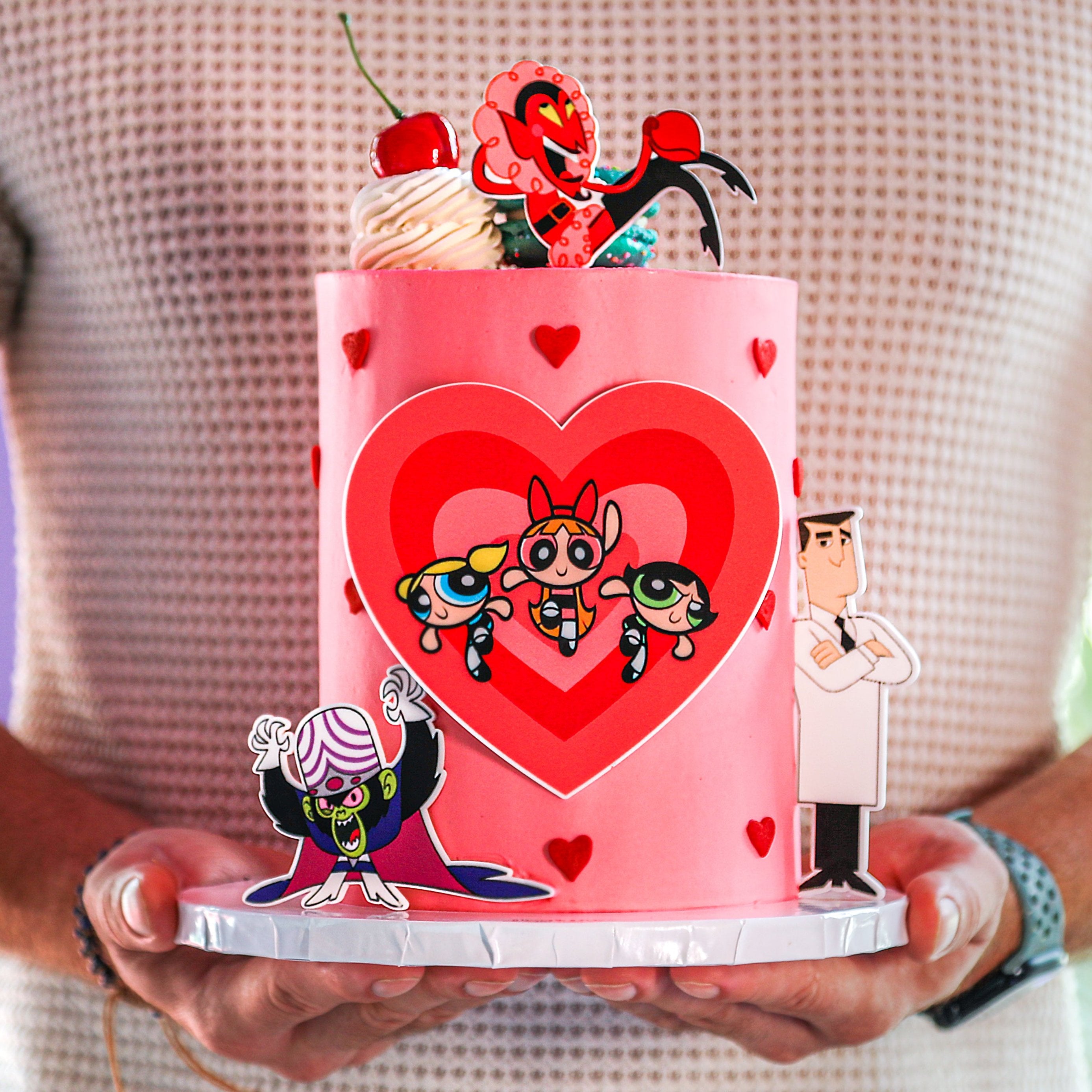 A decorated cake with characters from the Powerpuff Girls series, presented on a cake board.