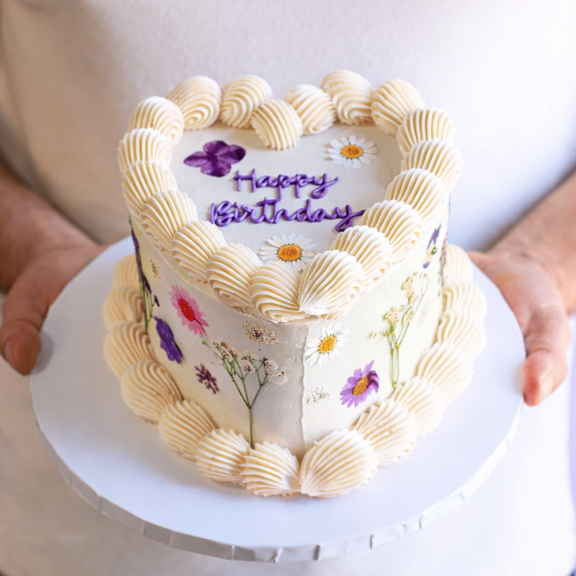 Heart-shaped birthday cake with floral decorations held by a person