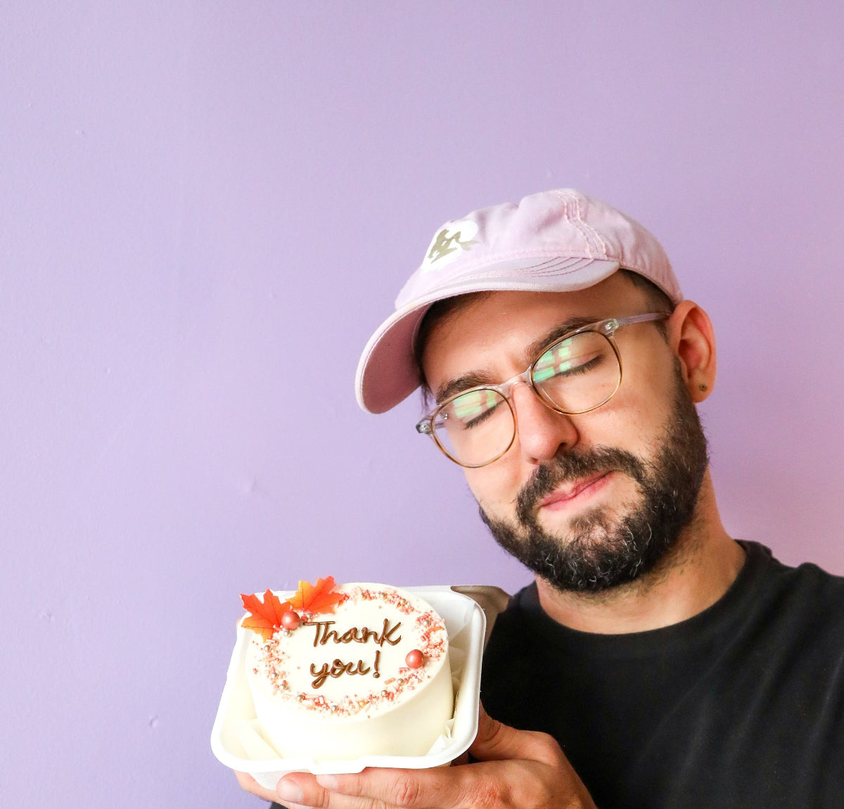 Handsome man holding a small cake with 'Thank you' on a purple background