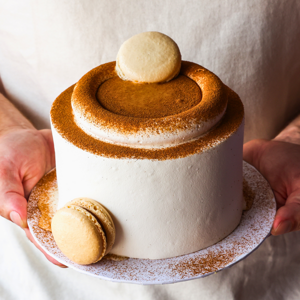 Small white cake with brown decorative elements held by a person
